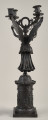Kandelabr 4 świecowy, ciemny w formie uskrzydlonej postaci na postumencie trzymającej w górze ramiona świecznika.