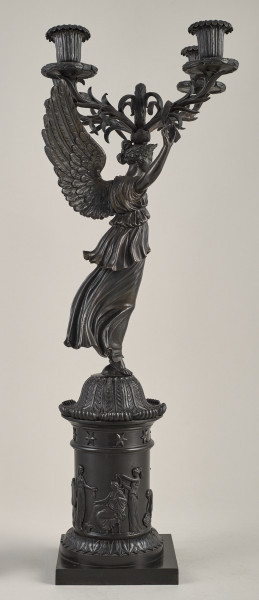 Kandelabr 4 świecowy, ciemny w formie uskrzydlonej postaci na postumencie trzymającej w górze ramiona świecznika.Bok lewy