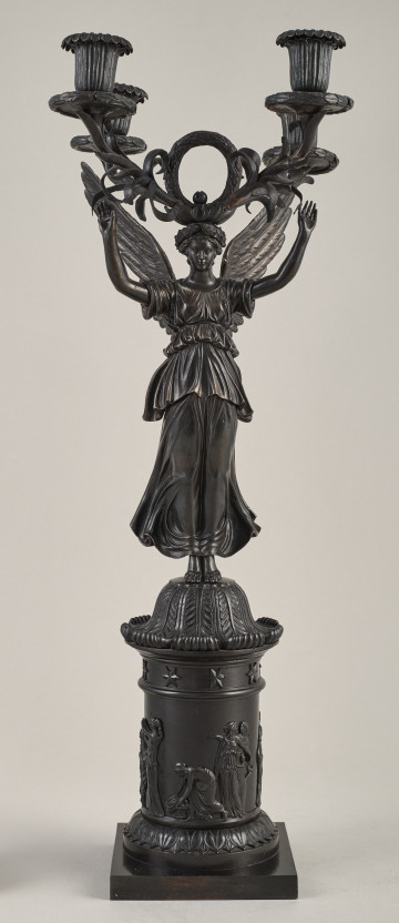 Kandelabr 4 świecowy, ciemny w formie uskrzydlonej postaci na postumencie trzymającej w górze ramiona świecznika.