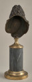 Jean Baptiste Racine. Brązowe, miniaturowe popiersie przedstawia go w starszym wieku, w peruce. Popiersie ustawione jest na podstawie złożonej z brązowego, złoconego cokoliku, cylindrycznego marmurowego trzonu (brak metalowego łańcuszka) i brązowej, złoconej bazy. Tył