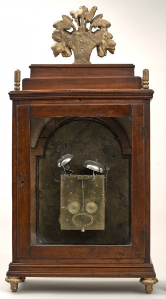 Zegar kominkowy w drewnianej obudowie ze złoceniami. Tylna strona z otwieranymi szklonymi drzwiczkami, przez które widać mechanizm.