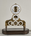 Zegar Roland z pięcioma porcelanowymi tarczami. Mechanizm został umieszczony na owalnej mahoniowej podstawie wspartej na czterech nóżkach.