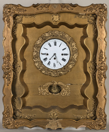 Zegar wiszący, złocony w formie przeszklonej otwieranej szafki w ramie ozdobnej. Biała tarcza zegarowa ozdobiona wieńcem rzeźbionym. Poniżej tarczy otwór.