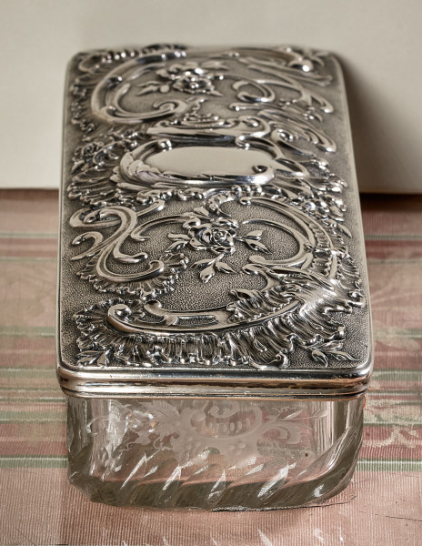 ﻿Kasetka ze szkła kryształowego i srebra. Ujęcie od strony węższej. Pokrywa srebrna bogato dekorowana.
