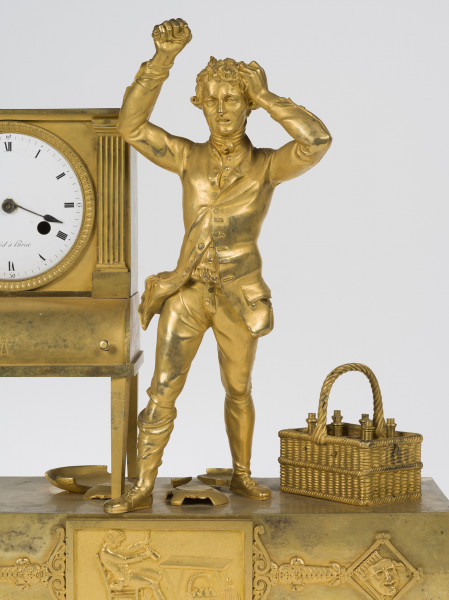zbliżenie na dekoracyjną obudowę zegara z brązu złoconego przedstawiającą pijanego mężczyznę stojącego obok sekretarzyka, pośród potłuczonych talerzy