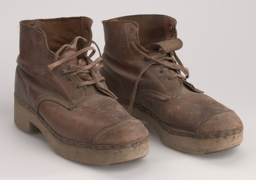 Ujęcie od przodu. Para butów męskich, skórzanych, wiązanych na drewnianej podeszwie.