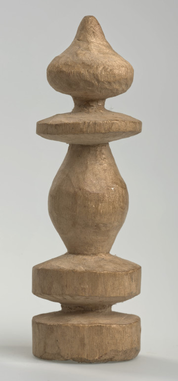 Ujęcie z boku [1]. Ze względu na swój okrągły kształt kolejne ujęcia z boku nie różnią się między sobą znacząco. Hetman został wykonany ręcznie z kawałka jasnego drewna. Na całej powierzchni widoczne są ślady rzeźbienia przy pomocy noża. Obiekt w kolorze naturalnego drewna (nie został pomalowany, ani polakierowany). Od spodu widoczne oznaczenie składające się z dwóch przecinających się ze sobą linii („X”), które umożliwia podzielenie bierek pomiędzy dwóch graczy - wszystkie bierki są jednakowego koloru. Hetman składa się ze spłaszczonej podstawy w formie krążka, środkowej części w formie walca rozszerzającego się po środku wysokości, dwóch spłaszczonych cylindrycznych elementów, które zwężają się stopniowo ku górze oraz ku dołowi (przypominając dwa połączone ze sobą talerze, z których każdy skierowany jest dnem do zewnątrz; elementy są umieszczone bezpośrednio jednej nad drugim przy podstawie oraz pod zwieńczeniem) oraz zwieńczenia o bulwiastym kształcie.