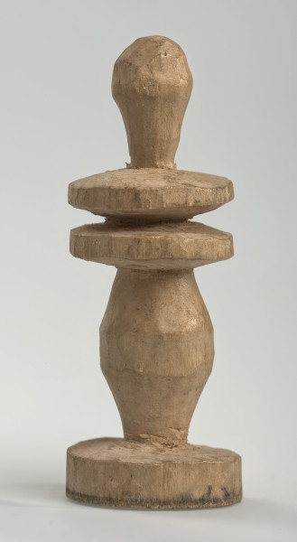 Ujęcie z boku [1]. Ze względu na swój okrągły kształt kolejne ujęcia z boku nie różnią się między sobą znacząco. Goniec został wykonany ręcznie z kawałka jasnego drewna. Na całej powierzchni widoczne są ślady rzeźbienia przy pomocy noża. Obiekt w kolorze naturalnego drewna (nie został pomalowany, ani polakierowany). Od spodu widoczne oznaczenie składające się z dwóch przecinających się ze sobą linii („X”), które umożliwia podzielenie bierek pomiędzy dwóch graczy - wszystkie bierki są w jednakowym kolorze. Krawędź podstawy została dodatkowo obrysowana ołówkiem. Goniec składa się ze spłaszczonej podstawy w formie krążka, środkowej części w formie walca rozszerzającego się po środku wysokości, dwóch spłaszczonych cylindrycznych elementów, które zwężają się stopniowo ku górze oraz ku dołowi (przypominając dwa połączone ze sobą talerze, z których każdy skierowany jest dnem do zewnątrz; elementy są umieszczone bezpośrednio jednej nad drugim) oraz zwieńczenia o prostej, rozszerzającej się ku górze formie (przypominającej pałkę).