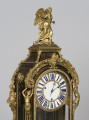 zbliżenie na górną część zegara - figura na szczycie (uskrzydlona postać kobieca), personifikacje pór roku na narożnikach szafki, tarcza zegara