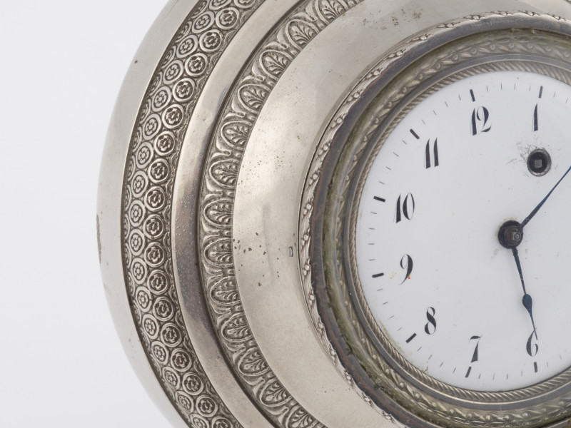zbliżenie na obudowę zegarka - metalowa profilowana rama, dekorowana motywami empirowymi