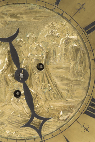 zbliżenie na dekoracyjną tarczę stanowiącą korpus zegara - ozdobiona w centrum płaskorzeźbioną, złoconą sceną biblijną przedstawiającą znalezienie przez córkę faraona małego Mojżesza w koszu płynącym po Nilu