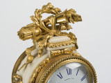 zbliżenie na dekoracyjne zwieńczenie obudowy zegara - pełnoplastyczna kompozycja z wieńca laurowego, kołczanu ze strzałami oraz płonącej pochodni przewiązana karbowaną wstęgą
