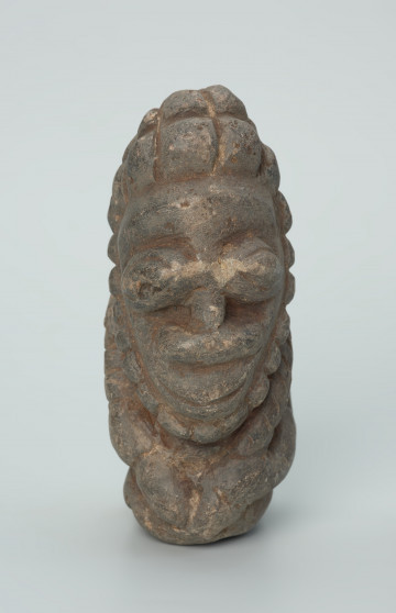 rzeźba; przedmiot obrzędowy; Figura kultu zmarłych - Ujęcie z przodu. Rzeźbiona w szarobeżowym steatycie siedząca postać ludzka o cechach męskich, w prawej dłoni trzymajaca przedmiot przypominający grot, a w lewej pióro lub liść.