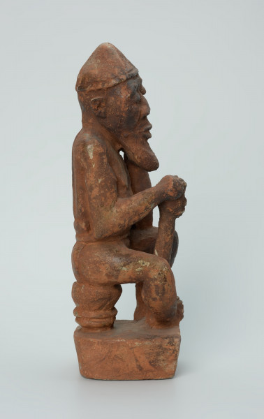 Ujęcie prawego boku. Rzeźbiona w brunatno-czerwonym kamieniu dość duża postać mężczyzny (starca?) w pozycji siedzącej. Mężczyzna siedzi na okrągłym, malutkim stołku, ma charakterystyczne nakrycie głowy - spiczastą czapkę o zaokrąglonych rogach. Jego prawa ręka opiera się o berło (laskę) zakończone rzeźbą głowy. Widoczne rysy, mikropęknięcia i liczne malutkie otworki.
