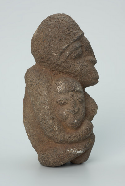 rzeźba; przedmiot obrzędowy; figura kultu zmarłych - Ujęcie prawy bok. Rzeźbiona w ziemistym steatycie siedząca postać kobiety z wyłaniającymi się symetrycznie zza jej boków dwoma ludzkimi głowami.