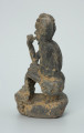 figura kultu przodków - Ujęcie z boku z lewej. Rzeźbione w grafitowym kamieniu dwie złączone ze sobą postaci ludzkie w pozycji siedzącej. Stykają się ramionami, tułowiem oraz nogami. Jedna z nich – najprawdopodobniej mężczyzna - trzyma w prawej dłoni fajkę. Rzeźba pokryta jest piaskiem. Widoczne rysy, mikropęknięcia, malutkie otworki, przebarwienia oraz ślady klejenia w okolicach szyi.