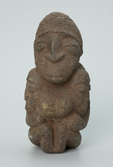 rzeźba; przedmiot obrzędowy; figura kultu zmarłych - Ujęcie z przodu. Rzeźbiona w ziemistym steatycie siedząca postać kobiety z wyłaniającymi się symetrycznie zza jej boków dwoma ludzkimi głowami.