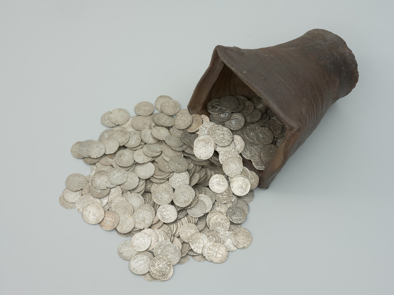 skarb monet - Ujęcie naczynia z wysypującymi się monetami z góry. Skarb 656 szelągów krzyżackich i 2 guldenów niemieckich ukryty w kaflu piecowym pod koniec XV wieku.