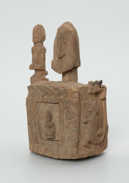 drewniane pudełko na fetysz - Ujęcie z przodu, z lewej strony. Drewniane pudełko, dekorowane płaskorzeźbami, w środku którego widoczne są drzwiczki.