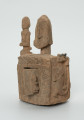 drewniane pudełko na fetysz - Ujęcie z przodu, z lewej strony z otwartymi drzwiczkami. Drewniane pudełko, dekorowane płaskorzeźbami, w środku którego widoczne są drzwiczki.