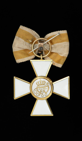 Order Czerwonego Orła III klasy - Ujęcie rewersu. Krzyż maltański biało emaliowany z czerwonym orłem w środkowym medalionie. Na rewersie w środkowym medalionie na białej emalii ukoronowany królewski monogram FW. U góry uszko, w którym okrągła zawieszka i wstążka żółto-biała.