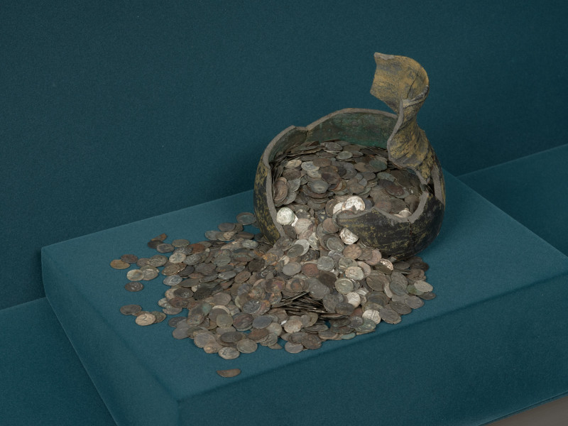 skarb monet - Ujęcie z przodu. Fragment glinianego naczynia z wysypującymi się z niego monetami. Skarb 2588 monet, głównie denarów pomorskich, ukryty w naczyniu glinianym po 1405-1410 roku.