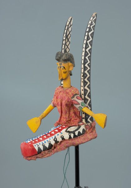 lalka teatralna: Yayoroba na antylopie dajè - Ujęcie z przodu z lewej strony. Drewniana lalka teatralna przedstawiającą kobietę siedzącą na głowie antylopy.