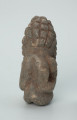 rzeźba; przedmiot obrzędowy; Figura kultu zmarłych - Ujęcie z tyłu. Rzeźbiona w szarobeżowym steatycie siedząca postać ludzka o cechach męskich, w prawej dłoni trzymajaca przedmiot przypominający grot, a w lewej pióro lub liść.