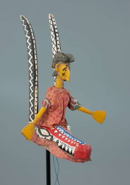 Ujęcie z przodu z prawej strony. Drewniana lalka teatralna przedstawiającą kobietę siedzącą na głowie antylopy.