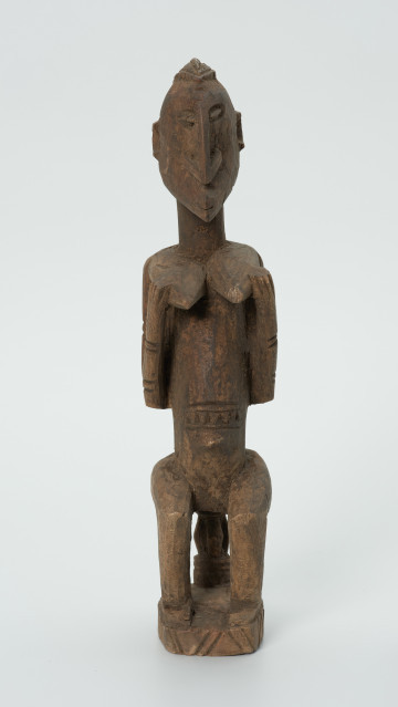 drewniana, rzeźbiona figura - Ujęcie z przodu. Drewniana, rzeźbiona figura kobiety siedzącej na stołku.