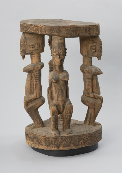 rzeźba - Ujęcie z tyłu z lewej strony. Drewniany stół. Okrągły blat połączony z podstawą o tym samym kształcie za pomocą czterech rzeźbionych postaci.