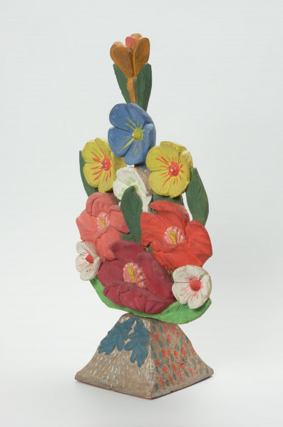 rzeźba - Ujęcie z przodu skosem w prawą stronę. Bukiet kwiatów wykonany w drewnie jako spłaszczona kompozycja rzeźbiarska opracowana jedynie po stronie frontalnej. Rozłożenie kompozycji symetryczne względem osi pionowej. Kwiaty przedstawione są w trzech układach wertykalnych. 