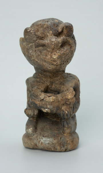 rzeźba; przedmiot obrzędowy; Figura kultu sił wegetacji - Ujęcie z przodu. Rzeźbiona w białoszarym steatycie siedząca na płaskiej, owalnej podstawie kobieta trzymająca w dłoniach, przy biuście zwrócone ku niej dziecko.