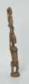 drewniana, rzeźbiona figura - Ujęcie z przodu, z prawej strony. Drewniana, rzeźbiona figura przedstawiająca postać człowieka niosącego na plecach drugą osobę.