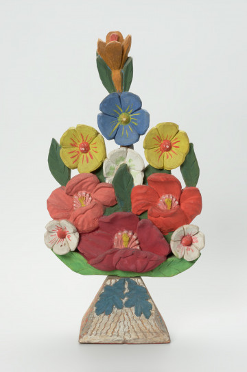 rzeźba - Ujęcie z przodu. Bukiet kwiatów wykonany w drewnie jako spłaszczona kompozycja rzeźbiarska opracowana jedynie po stronie frontalnej. Rozłożenie kompozycji symetryczne względem osi pionowej. Kwiaty przedstawione są w trzech układach wertykalnych. 