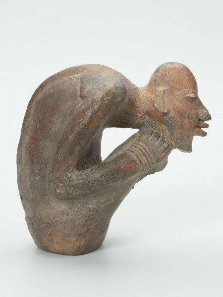 figura - Ujęcie z boku z prawej; Gliniana rzeźba postaci ludzkiej w kolorze beżowo-brązowo-ceglastym. Postać w pozycji siedzącej, mocno pochylona do przodu. Twarz oparto na prawej dłoni, która usytuowana została na prawym kolanie. Rzeźbie nie zachowały się w całości nogi (prawa poniżej kolana, lewa poniżej uda) oraz lewe przedramię i dłoń. Postaci zaznaczono bardzo wyraźną linię kręgosłupa.