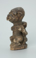 rzeźba; przedmiot obrzędowy; Figura kultu sił wegetacji - Ujęcie z przodu z lewej strony. Rzeźbiona w grafitowym steatycie siedząca postać ludzka o cechach kobiecych z podkurczonymi nogami i dzieckiem na plecach.