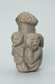 rzeźba; przedmiot obrzędowy; figura kultu zmarłych - Ujęcie z tyłu. Rzeźba o gładkiej powierzchni w szarym steatycie, przedstawiająca postać ludzką o cechach kobiecych, otoczoną piątką mniejszych, dziecięcych sylwetek w różnych pozach.