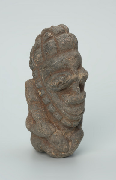 rzeźba; przedmiot obrzędowy; Figura kultu zmarłych - Ujęcie z przodu z prawej strony. Rzeźbiona w szarobeżowym steatycie siedząca postać ludzka o cechach męskich, w prawej dłoni trzymajaca przedmiot przypominający grot, a w lewej pióro lub liść.