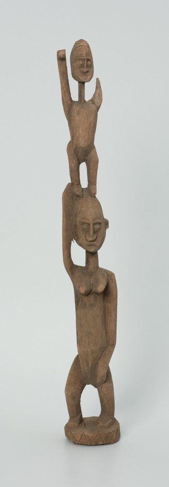 drewniana, rzeźbiona figura - Ujęcie z przodu. Drewniana, rzeźbiona figura przedstawiająca postać człowieka niosącego na plecach drugą osobę.
