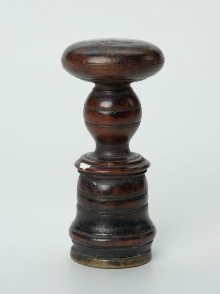 łłok pieczętny - Ujęcie z boku; Okrągły tłok pieczętny z brązu z drewnianym uchwytem oraz rysunkiem łba wołu i skrzyżowanych toporów w polu pieczęci.