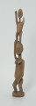 drewniana, rzeźbiona figura - Ujęcie z przodu, z lewej strony. Drewniana, rzeźbiona figura przedstawiająca postać człowieka niosącego na plecach drugą osobę.
