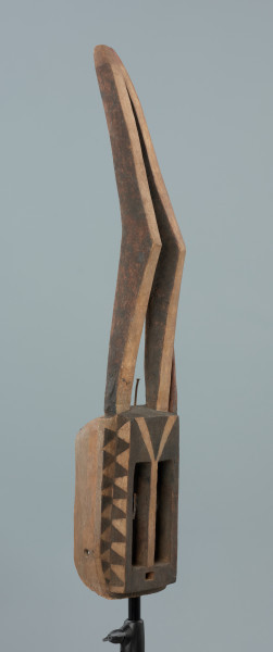 maska - Ujęcie z przodu, z prawej strony. Drewniana, rzeźbiona maska antylopy, z dużymi geometrycznymi otworami na oczy.