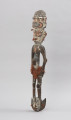 hak do wieszania toreb - Ujęcie ze skosu z lewej; Drewniany hak z postacią ludzką (najprawdopodobniej kobietą) w górnej części i kotwicowym zaczepem z wyrzeźbioną głową ludzką w dolnej części. Hak polichromowany, bogato zdobiony