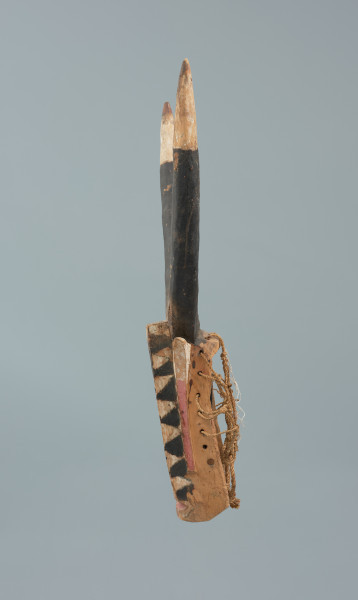 rzeźbiona maska - Ujęcie lewego boku. Drewniana, rzeźbiona maska byka, do której przymocowany jest bawełniany sznurek.