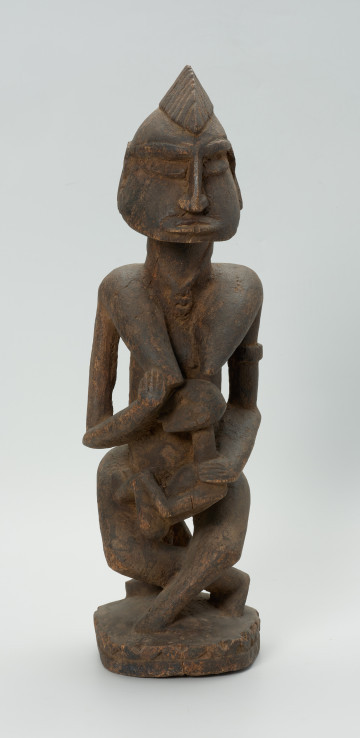 drewniana, rzeźbiona figura - Ujęcie z przodu. Drewniana, rzeźbiona postać kobiety, trzymającej w ramionach małe dziecko.