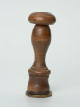 tłok pieczętny - Ujęcie z boku; Okrągły tłok pieczętny z brązu z drewnianym uchwytem oraz rysunkiem buta z dwugłowym orłem w polu pieczęci.