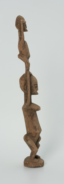 drewniana, rzeźbiona figura - Ujęcie prawego boku. Drewniana, rzeźbiona figura przedstawiająca postać człowieka niosącego na plecach drugą osobę.