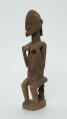drewniana, rzeźbiona figura - Ujęcie z przodu, z prawej strony. Drewniana, rzeźbiona figura kobiety siedzącej na stołku.