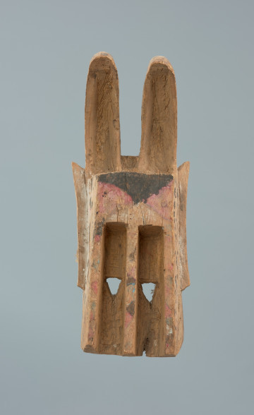 maska zająca - Ujęcie z przodu. Drewniana, rzeźbiona maska w kształcie zająca, którego  uszy wygięte są do przodu i wydrążone.